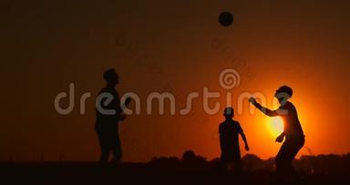 三个男孩在日落时踢足球。 日落时孩子们玩球的<strong>剪影</strong>。 幸福家庭的概念
